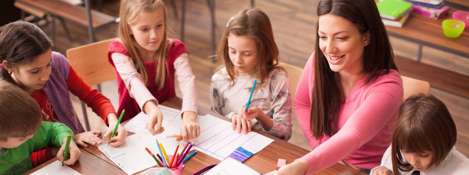 teacher works with students at table in elementary classroom